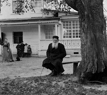 Л. Н. Толстой на лавочке у «дерева бедных» (вяз, под которым по утрам собирались люди, пришедшие к писателю за советом или с просьбой о помощи). На заднем плане С. А. Толстая и четверо крестьянских мальчиков. Ясная Поляна. 1908. Автор фото: П. Кулаков